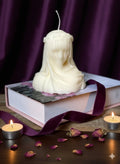 Ivory vanilla scented dimensional lady candle on a book with purple velvet ribbon and dried roses.