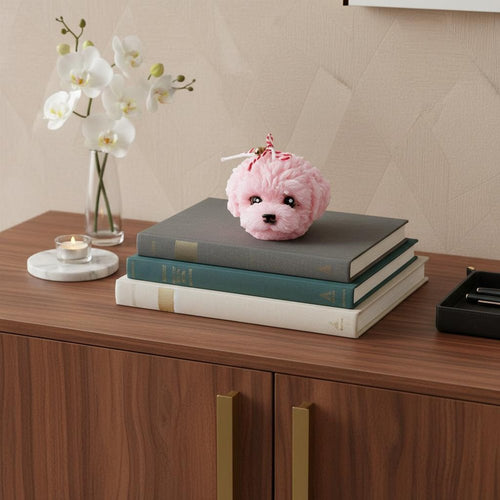Pink dimensional dog-shaped novelty candle on a stack of books with orchids and a lit candle in the background.