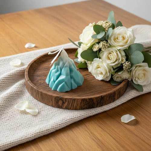 A blue and white dimensional iceberg candle on a wooden tray with a bouquet of white roses and eucalyptus on a wooden table.