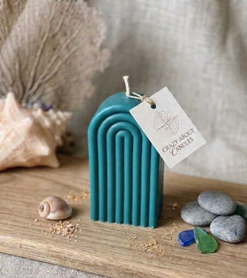 Teal arched candle with a tag that says "Crazy About Candles" on a wooden board with shells and stones.