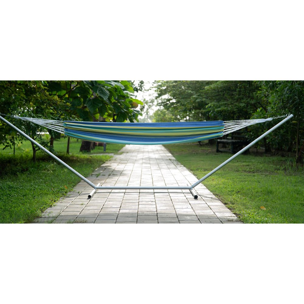 Blue, green, and yellow striped single spreader bar hammock on a white metal stand in a park setting.