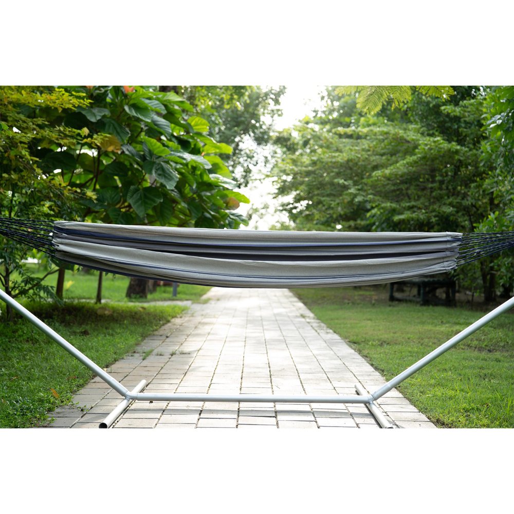 Gray striped hammock with spreader bars on a metal stand in a garden with a paved walkway.