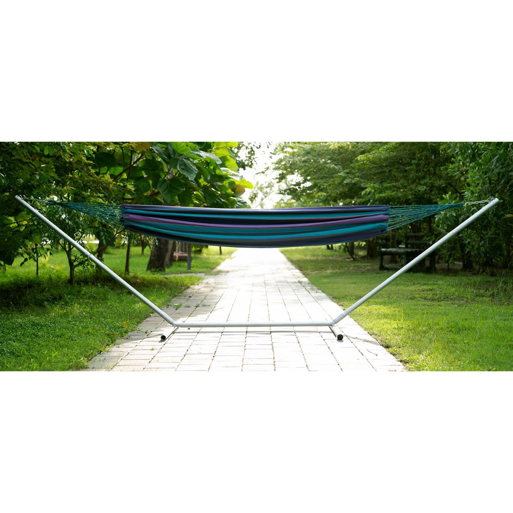 Striped hammock with blue, purple, and teal fabric on a white metal stand in a park setting.