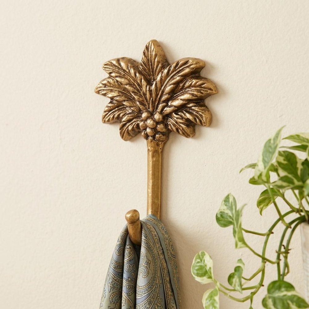 4" Antiqued Gold Cast Iron Palm Tree Wall Hook styled in a furnished interior with an off-white wall on the floor.