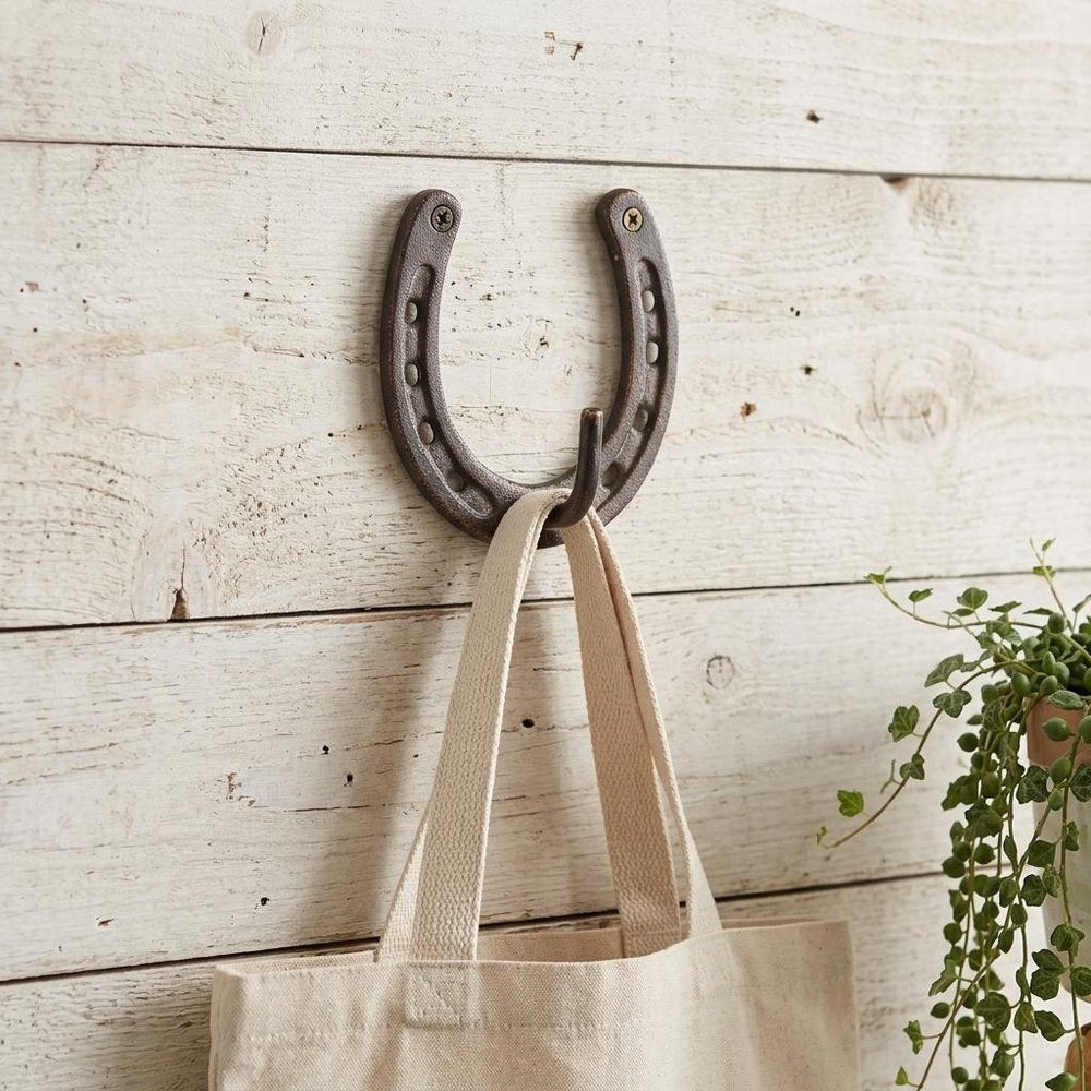 4" Antiqued Bronze Cast Iron Horseshoe Wall Hook styled in a furnished interior with an off-white wall on a wood floor.