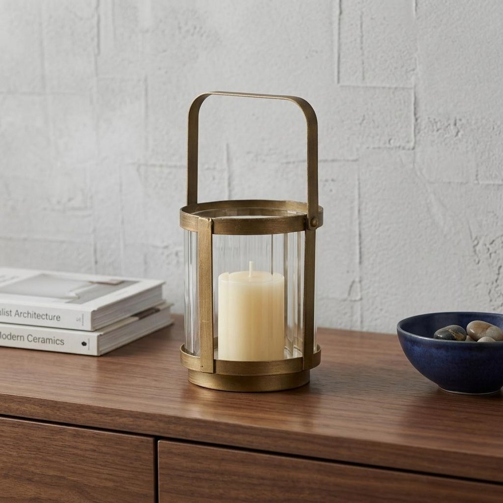 5" Gold Glass Tabletop Lantern Candle Holder displayed on a dark wood tabletop in a furnished interior against a light gray wall.