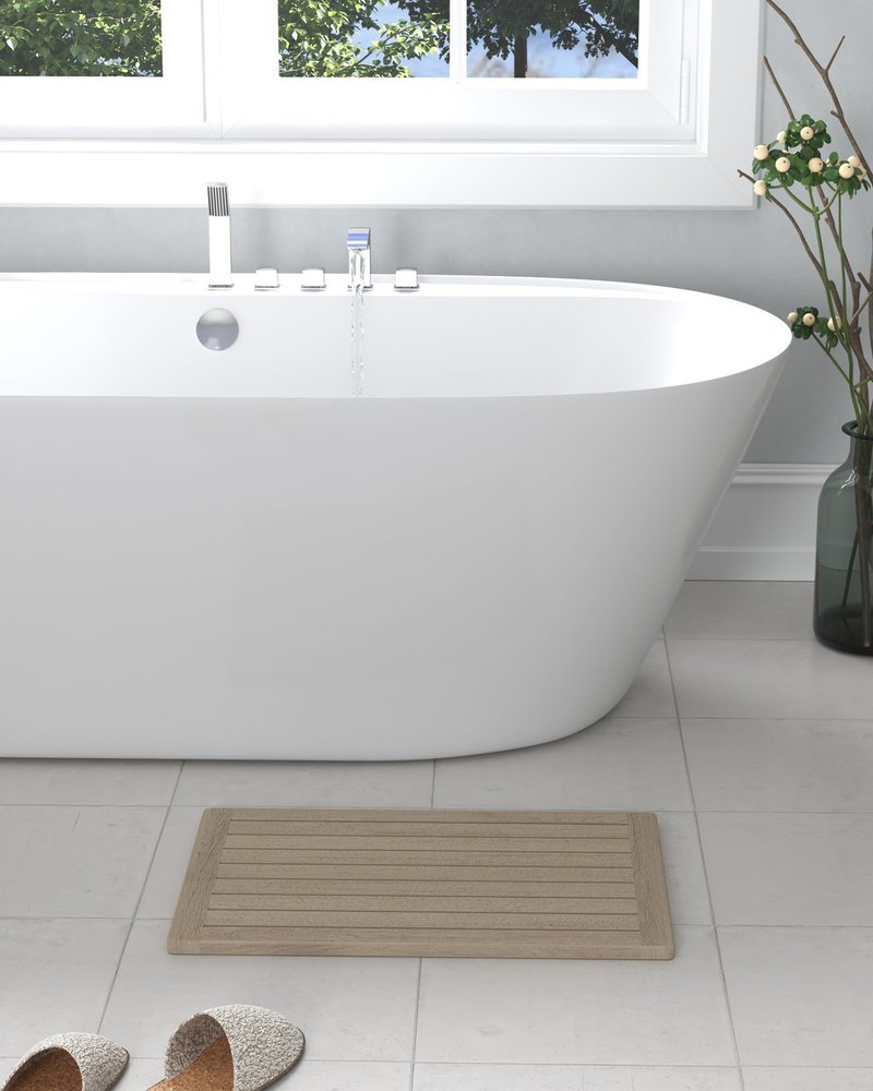 Beige gray teak non-slip bath mat with horizontal slats on a tiled bathroom floor next to a white bathtub.