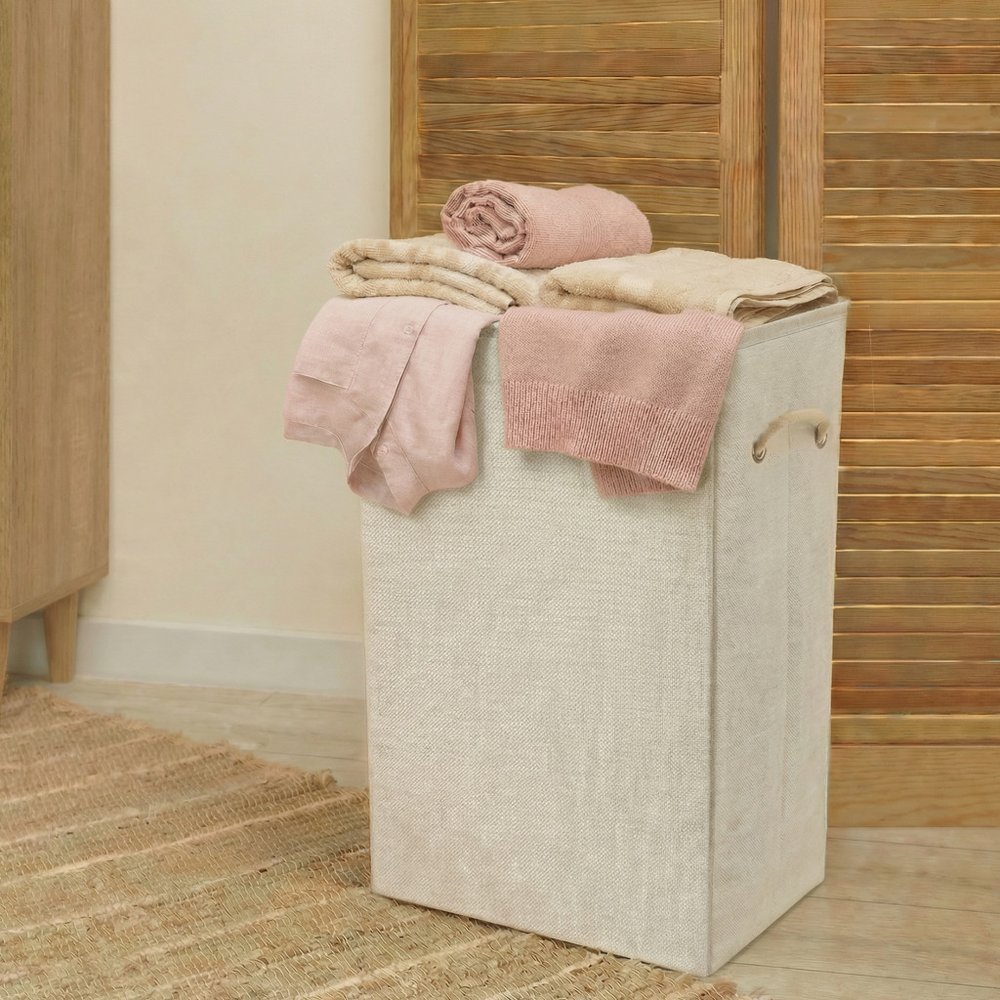 Off-white wicker laundry hamper with pink and beige folded clothes on top, in front of a wooden slatted door.
