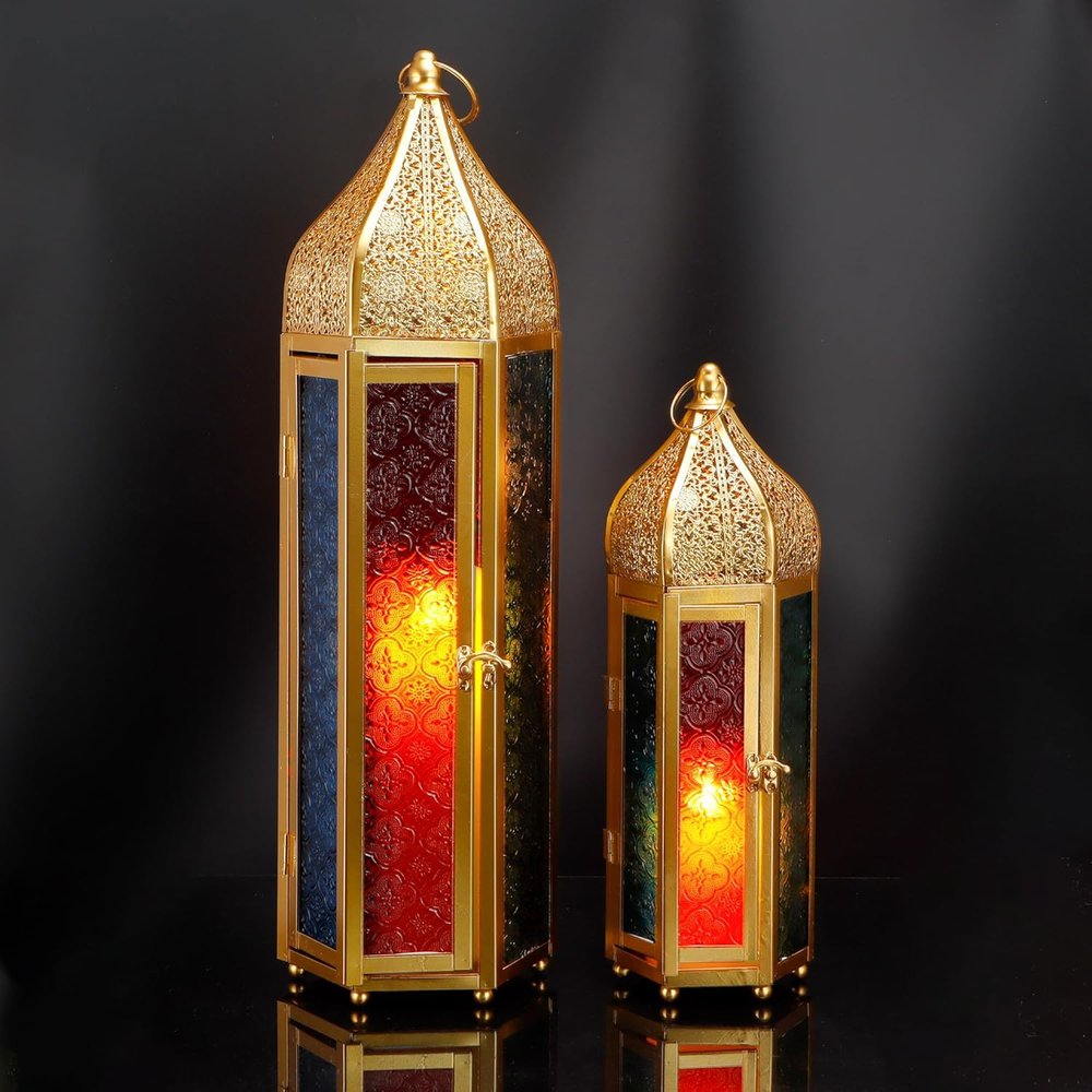 Two gold metal lanterns with distressed filigree tops and colored glass panels in blue, red, and green, lit from within, on a dark reflective surface.