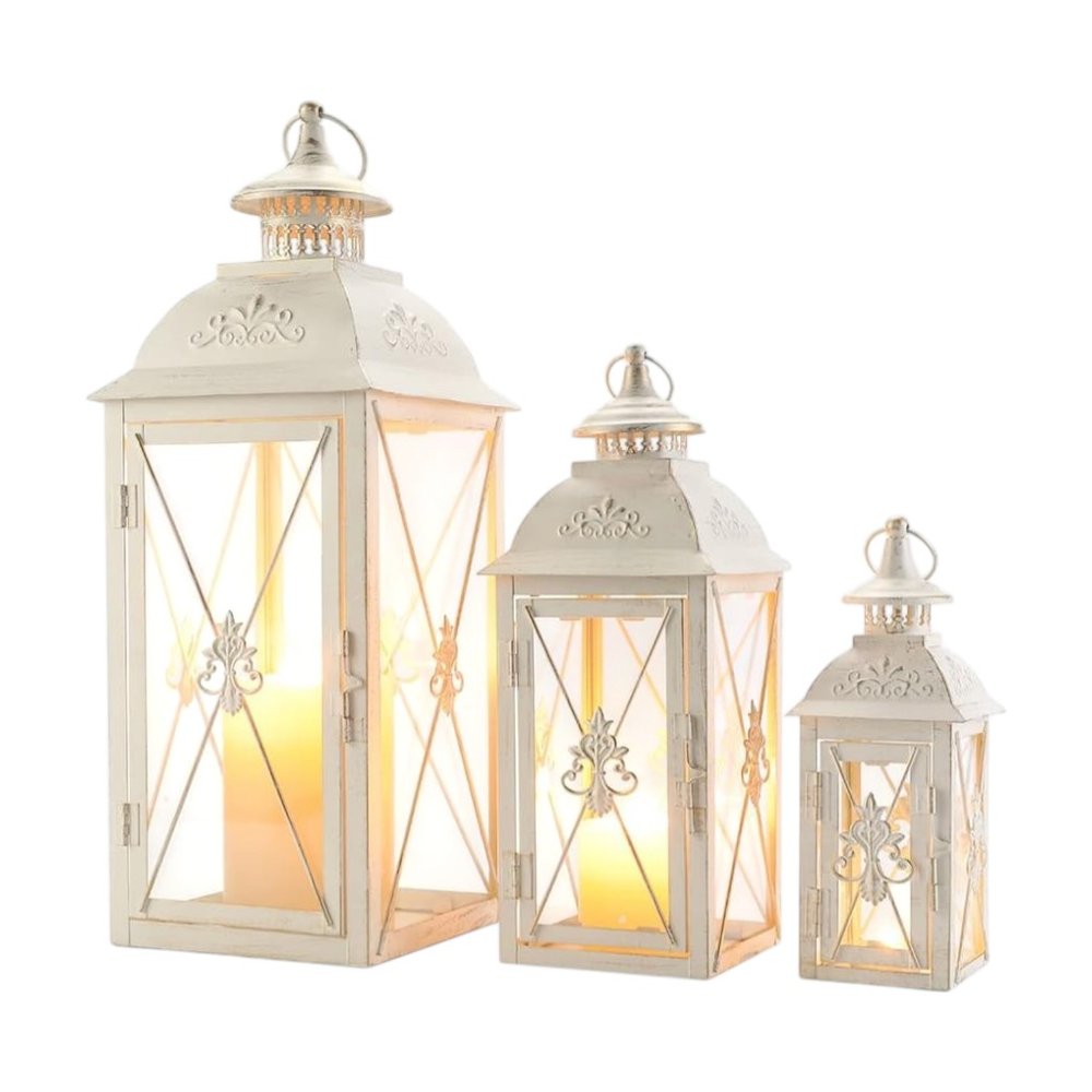 Set of three white metal and glass tabletop lanterns with filigree scroll details on a white background.