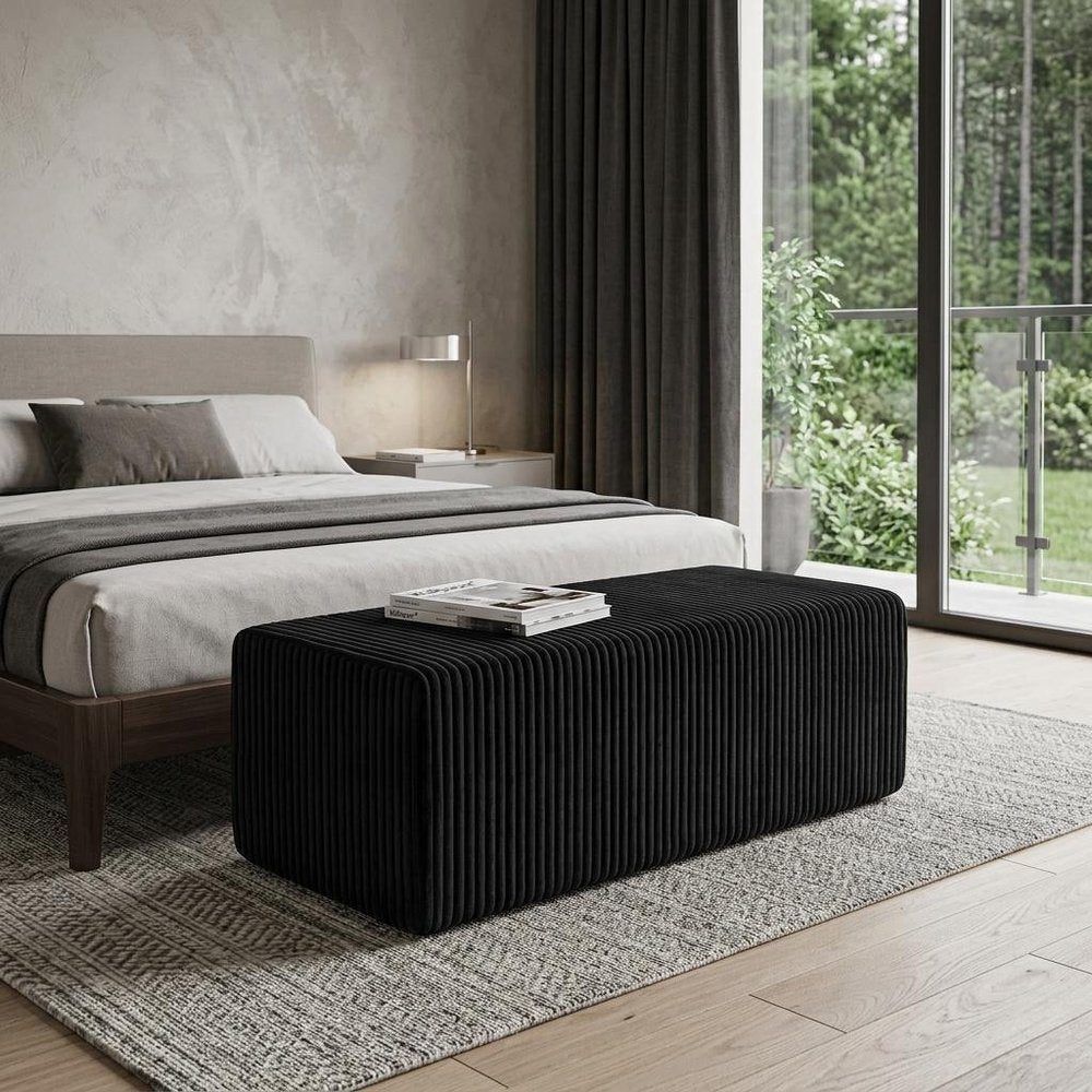 51" Black Corduroy Ottoman styled in a furnished interior with a gray wall on a tiled floor.
