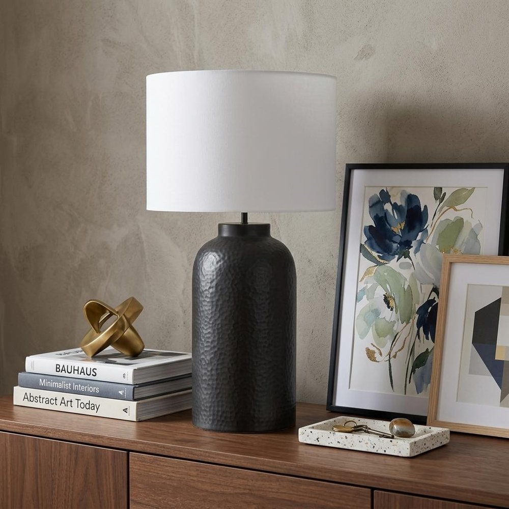 30" Black Novelty Table Lamp With Drum Shade displayed on a dark wood tabletop in a furnished interior against a tan wall.