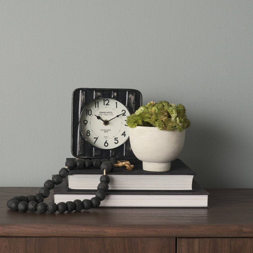 6" Black Metal Analog Round Wall Clock styled in a furnished interior with a light gray wall on a dark wood floor.