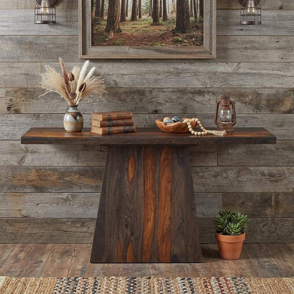 57" Mahogany and Dark Brown Solid Wood Pedestal Console Table styled in a furnished interior with a dark brown wall on a dark wood floor.