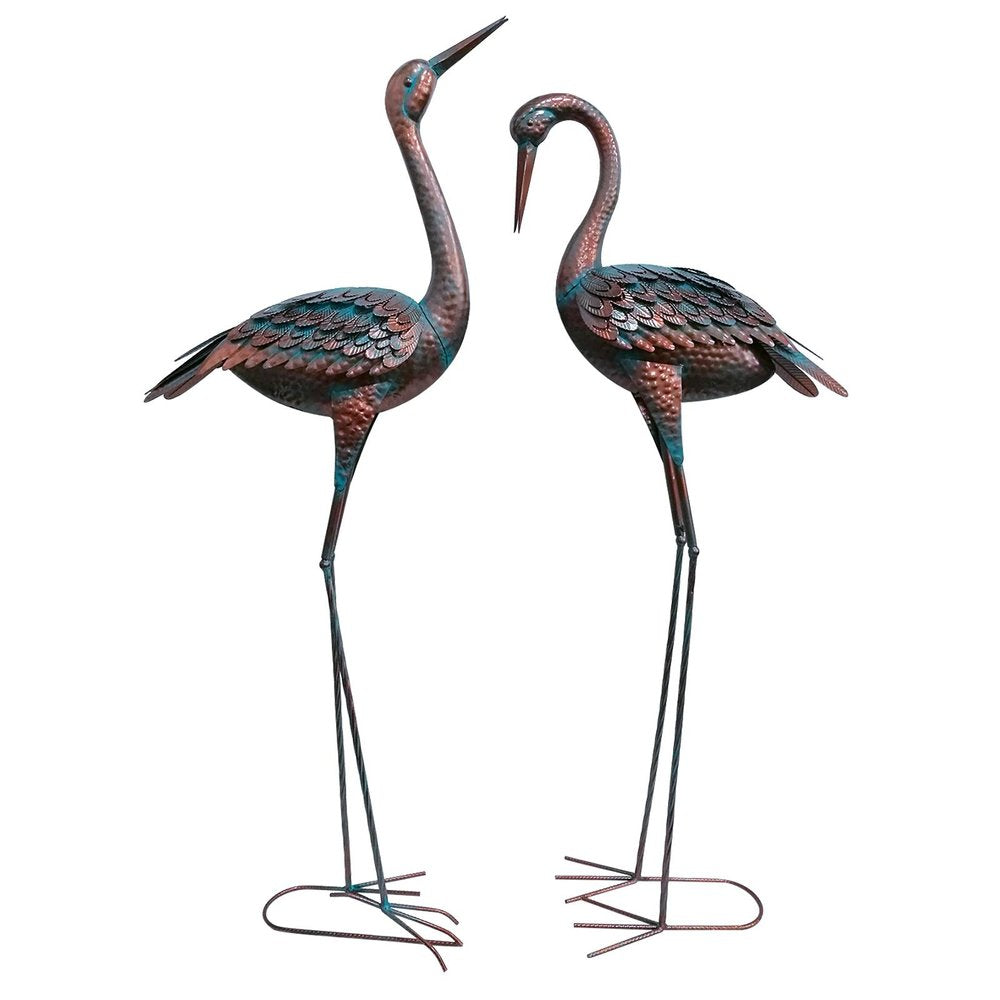 Two copper and green metal crane garden accents with long legs and textured bodies on a white background.