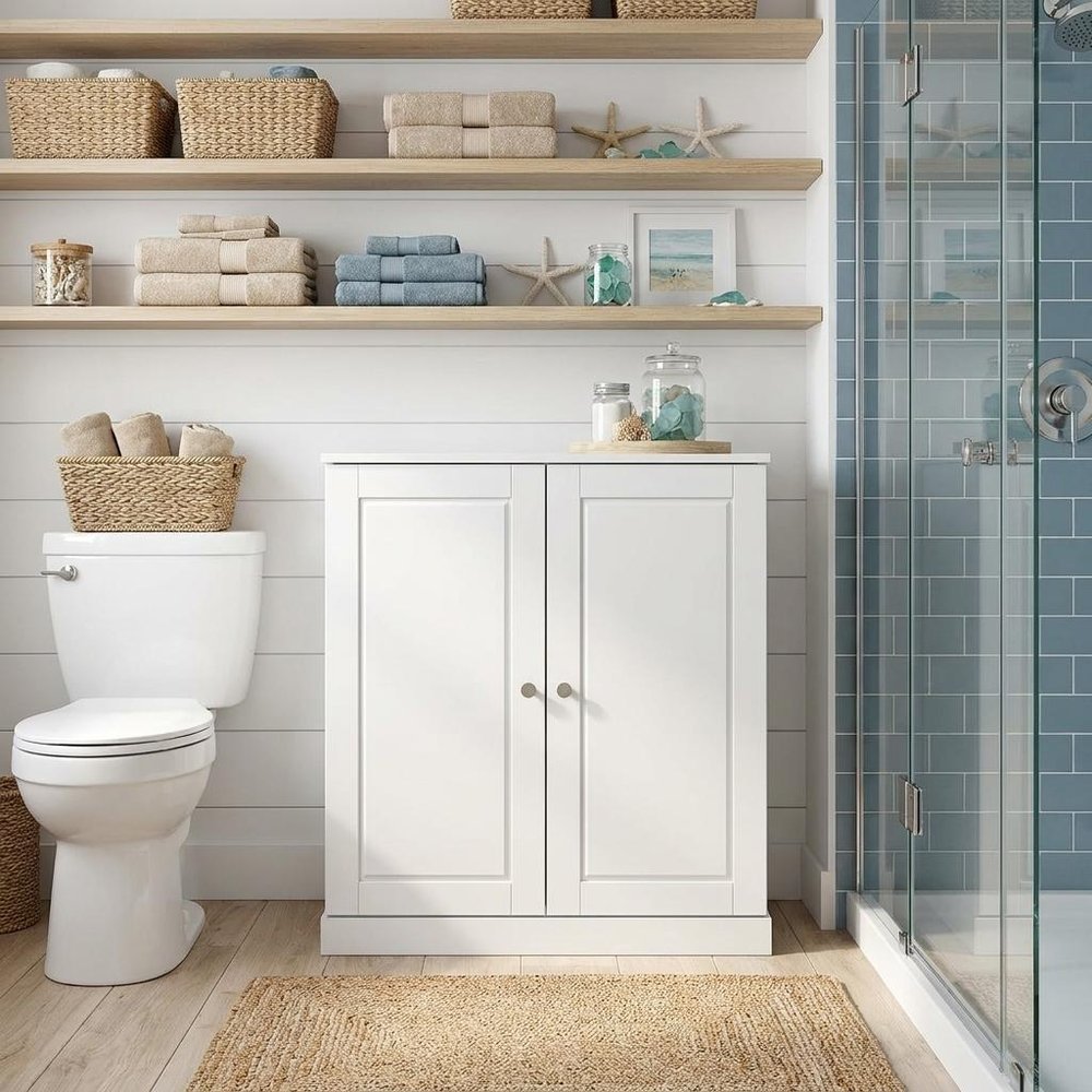 32" White Solid Wood Raised Panel Double Door Linen Cabinet styled in a furnished interior with a tan wall on a wood floor.