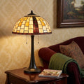24" Bronze Abstract Two Light Round Tiffany Lamp With Dome Shade styled in a furnished interior with a tan wall on a black floor.