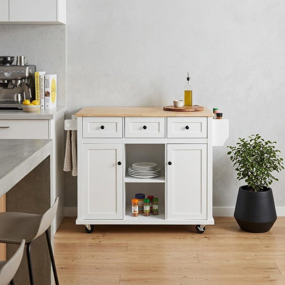 53" Brown and White Wood Flat Door Rolling Kitchen Cart With Storage styled in a furnished interior with an off-white wall on a wood floor.