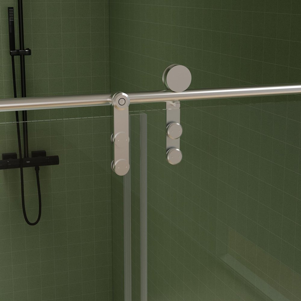 Chrome sliding shower door with clear glass panels against a green tiled wall.