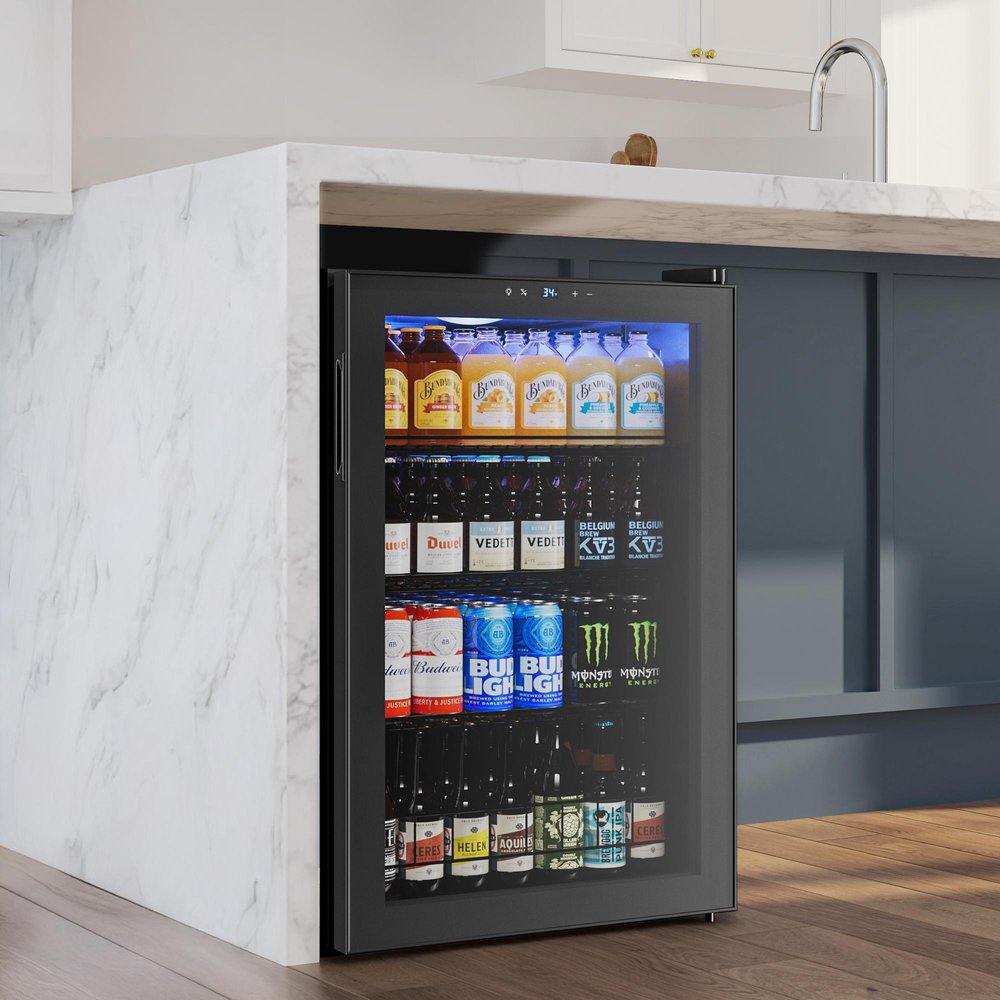 33" X 22" Clear and Black Stainless Steel Single Compartment Can Beverage Refrigerator styled in a furnished interior with a light gray wall on a dark wood floor.
