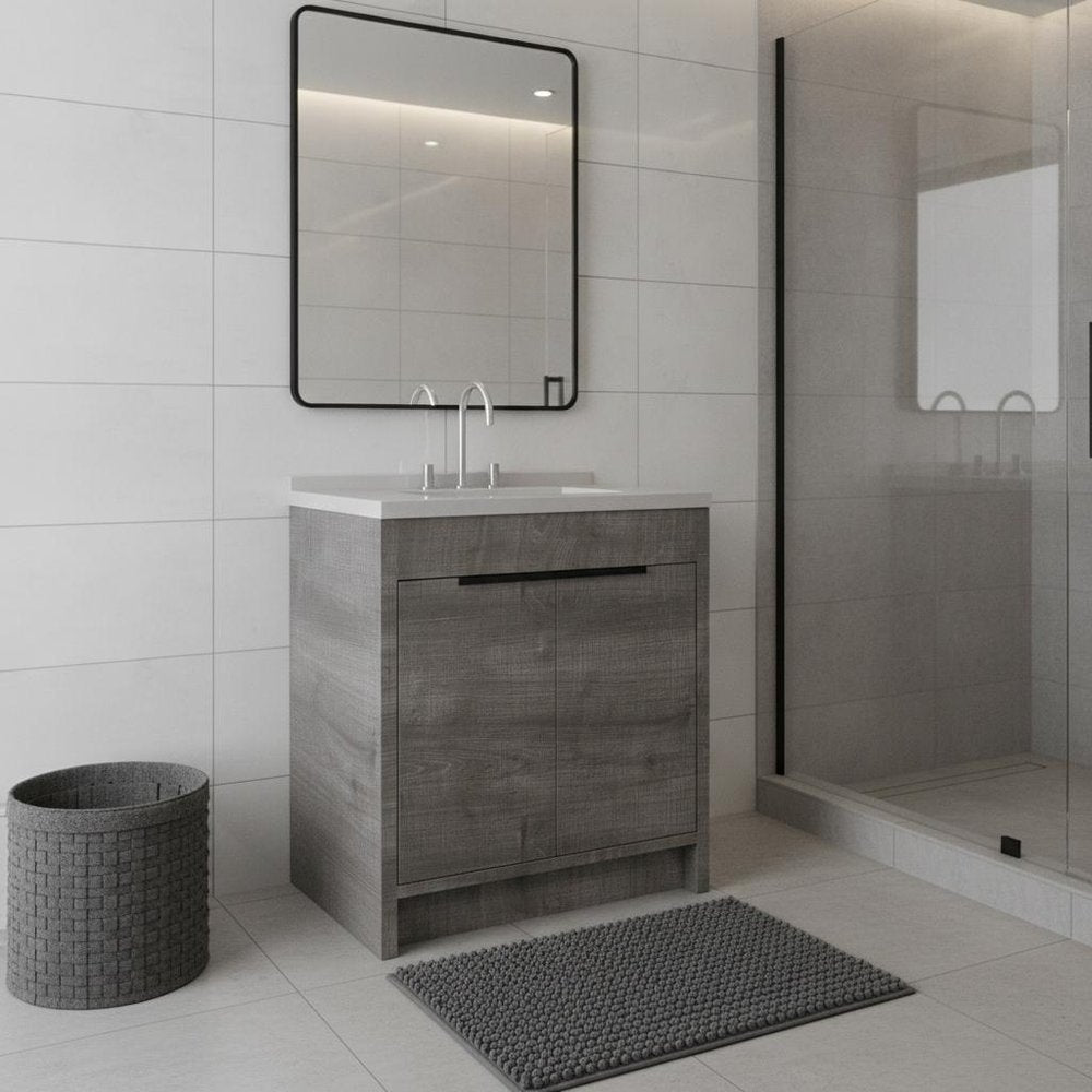 Gray wood freestanding bathroom vanity with white sink and black framed mirror in a tiled bathroom.