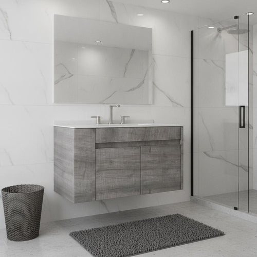 Gray wood floating bathroom vanity with white sink and chrome faucet against a marble tiled wall.